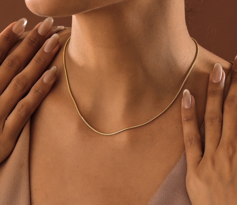 May include: A close-up of a woman's neck wearing a delicate gold chain necklace.