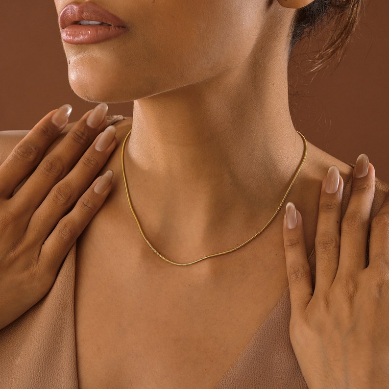May include: A close-up of a person wearing a gold chain necklace. The necklace is thin and delicate, and it is worn against the person's bare skin.