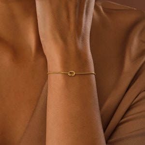 Peut inclure: Un bracelet en or avec un motif de n&oelig;ud. Le bracelet est fin et d&eacute;licat, et le n&oelig;ud est un design simple et &eacute;l&eacute;gant.
