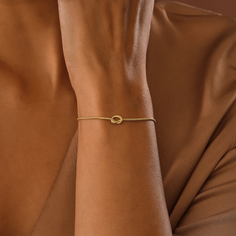 Peut inclure: Un bracelet en or avec un motif de n&oelig;ud. Le bracelet est fin et d&eacute;licat, et le n&oelig;ud est un design simple et &eacute;l&eacute;gant.