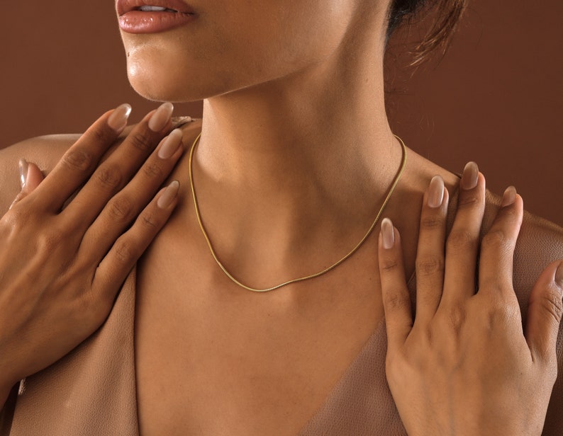 May include: A close-up of a person wearing a gold chain necklace. The chain is thin and delicate, and it is worn against the person's bare skin.