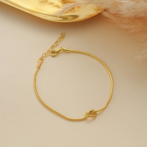 Peut inclure: Un bracelet dor&eacute; avec un motif de n&oelig;ud. Le bracelet est fait d'une fine cha&icirc;ne serpent.