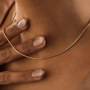 May include: A gold chain necklace on a person's neck. The chain is thin and delicate, and it is made of a smooth, shiny metal.