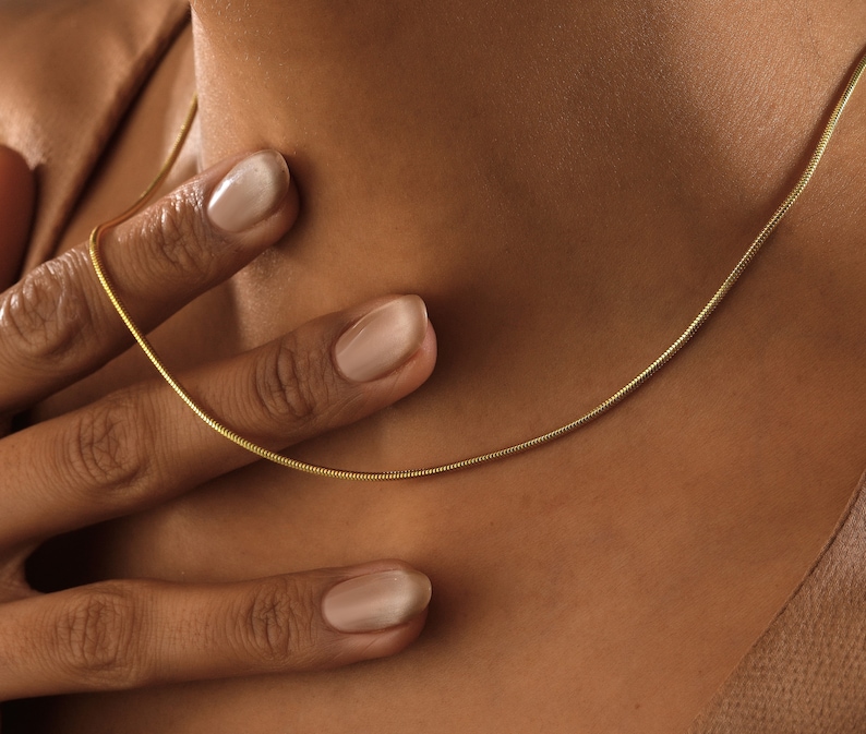 May include: A gold chain necklace on a person's neck. The chain is thin and delicate, and it is made of a smooth, shiny metal.