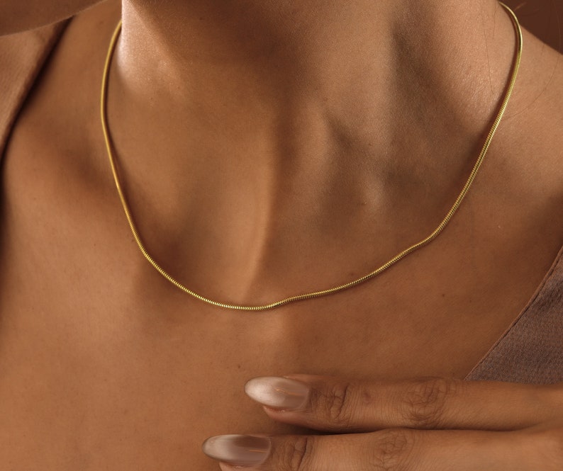May include: A gold chain necklace on a person's neck. The chain is thin and has a snake chain design.