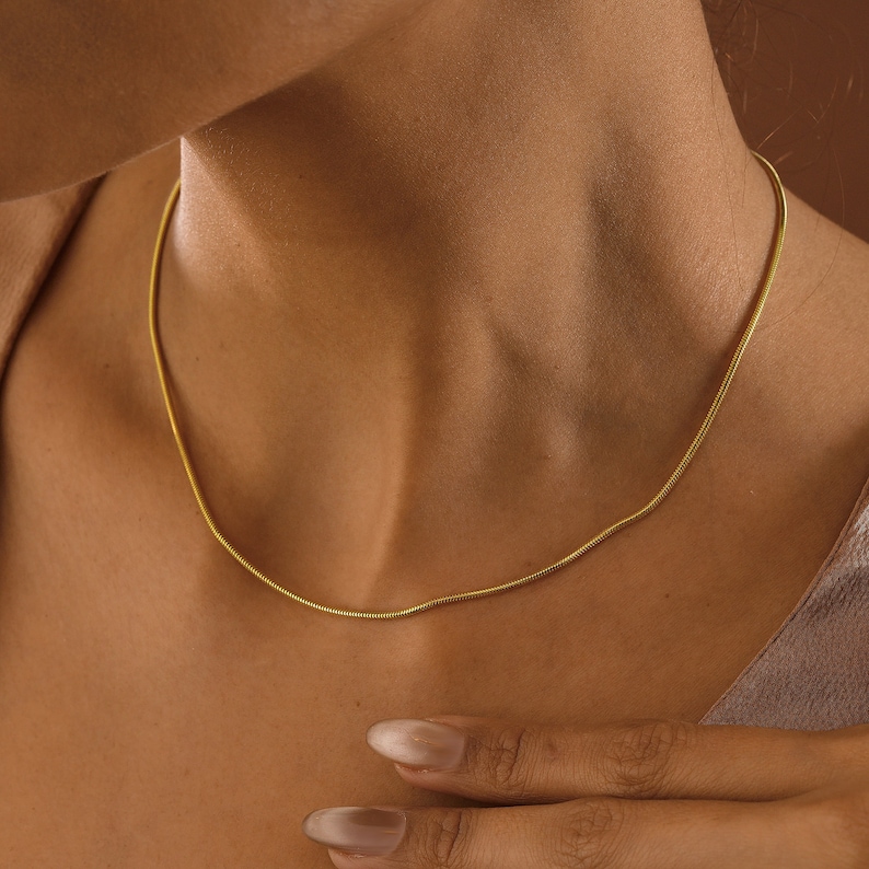 May include: A thin gold chain necklace on a person's neck. The chain is a simple, delicate design.