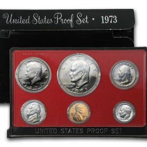 May include: A 1973 United States Proof Set in a black plastic case. The set includes six silver coins: a half dollar, a quarter, a dime, a nickel, a penny, and a half dime. The coins are arranged in a red plastic tray with the year 1973 printed on the tray.
