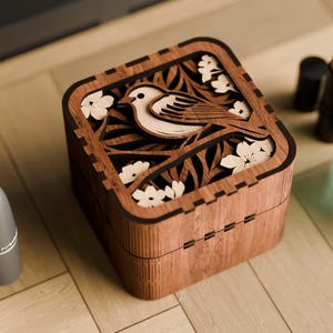 May include: A wooden box with a carved design of a bird and flowers. The box is made of dark wood and has a square shape.