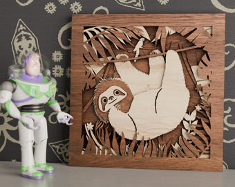 Könnte beinhalten: Ein Wandbild aus Holz mit einer detaillierten Ausschnitt eines Faultiers, das in einem Baum hängt. Das Faultier ist hellbraun und hat ein weißes Gesicht mit schwarzen Augen. Der Baum ist dunkelbraun und hat grüne Blätter.