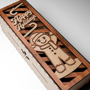 May include: Wooden box with a laser-cut gingerbread man and the words "Happy Holidays." The box is made of light and dark wood, with a diagonal striped pattern. The gingerbread man has a hat and scarf.