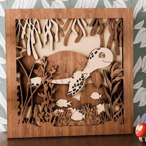 Op de afbeelding: Een houten wandkunstwerk dat een zeeschildpad afbeeldt die door een koraalrif zwemt. De schildpad is gedetailleerd gesneden en heeft een lichtbruine kleur. Het koraalrif is gemaakt van bruin hout en heeft verschillende vormen en maten. De achtergrond is van lichtbruin hout.