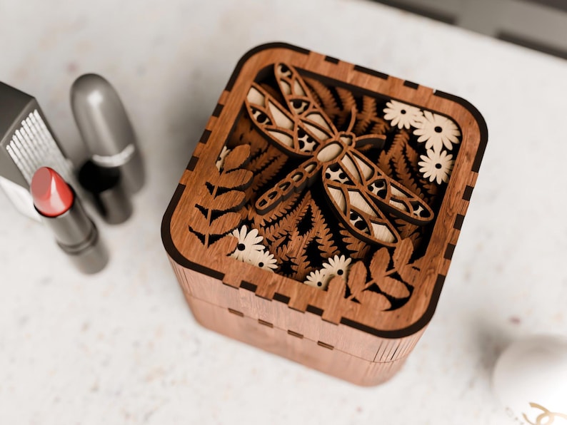 May include: A wooden box featuring a laser-cut design of a dragonfly and flowers. The box is crafted from dark wood and has a natural finish.