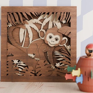 May include: A wooden wall decoration featuring a laser-cut design of a monkey in a jungle setting. The monkey is brown and has a white face with black eyes. The jungle scene is detailed with leaves, vines, and flowers.