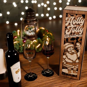 May include: A festive Christmas scene with a wine bottle, two wine glasses, and a wooden box with the words "Holly Jolly Christmas" and a Santa Claus design. A lit candle and fairy lights add to the holiday ambiance.