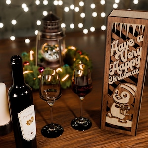 May include: A festive Christmas scene with a bottle of red wine, two wine glasses, and a wooden box with the text "Have a Very Happy Christmas" and a penguin design. A lit candle and fairy lights add to the holiday ambiance.