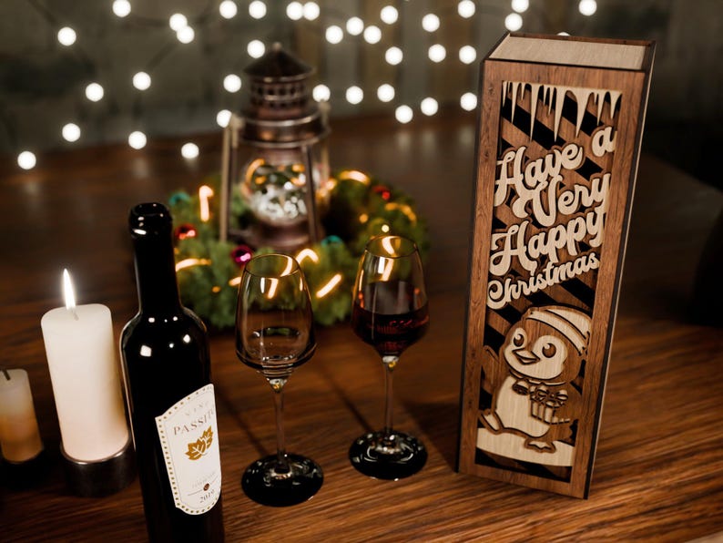 May include: A festive Christmas scene with a bottle of red wine, two wine glasses, and a wooden box with the text "Have a Very Happy Christmas" and a penguin design. A lit candle and fairy lights add to the holiday ambiance.