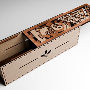 May include: Wooden box with a hinged lid, featuring a laser-cut design of a penguin holding gifts, and the words "Have a Very Happy Christmas." The box is light brown with darker brown accents.