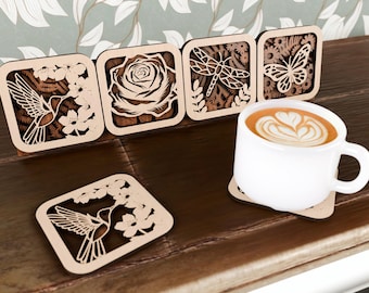 May include: Wooden square coasters with laser-cut designs of a hummingbird, rose, dragonfly, and butterfly. A white coffee cup with latte art sits on a matching coaster. The coasters are displayed on a dark wooden surface.