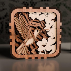May include: A wooden box featuring a laser-cut design of a hummingbird in flight, surrounded by flowers and ferns. The box is brown with a dark brown frame.