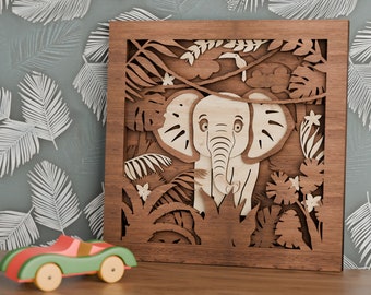 Könnte beinhalten: Ein Wandbild aus Holz mit einem ausgeschnittenen Design eines Elefanten in einer Dschungelkulisse. Der Elefant ist hellbraun und hat große Ohren und einen Rüssel. Die Dschungelszene besteht aus grünen Blättern und Blumen.