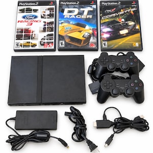 May include: A black PlayStation 2 game console with two black wired controllers, a power adapter, and two power cables. Included are three PlayStation 2 game cases titled Ford Racing 3, DT Racer, and Corvette, each featuring colorful car graphics.