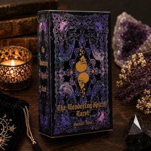 May include: A rectangular tarot deck box titled The Wondering Spirit Tarot by Haenuli Shin. The black box features intricate purple and blue filigree patterns, a central diamond shape containing two gold skulls, and gold lettering on the front.