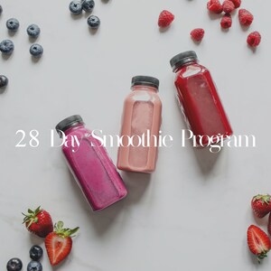 Op de afbeelding: Drie glazen flessen gevuld met roze, rode en paarse smoothies. De flessen staan op een wit marmeren oppervlak met blauwe bessen, frambozen en aardbeien die eromheen verspreid liggen. De tekst "28 Day Smoothie Program" staat in wit op het oppervlak.