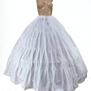 Op de afbeelding: Een witte crinoline petticoat met meerdere lagen, ontworpen om rokken volume te geven. De petticoat heeft een taille met trekkoord en is gemaakt van een lichte stof. Het wordt op een mannequin getoond.