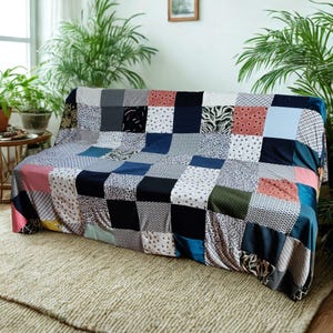 Op de afbeelding: Een rechthoekige bankhoes met een patchworkontwerp bestaande uit diverse stoffen vierkanten in uiteenlopende kleuren en patronen, waaronder effen marineblauw, zwart, lichtblauw, roze en olijfgroen, naast geometrische en bloemmotieven.