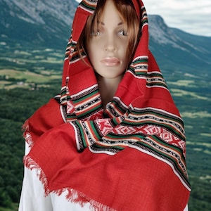 Può includere: Sciarpa rossa con bordo sfrangiato e bordo fantasia con strisce nere, bianche, verdi e rosse e motivi geometrici. La sciarpa è drappeggiata su una camicia bianca e una testa di manichino.