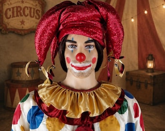May include: A clown costume featuring a white long-sleeve shirt with large red, yellow, blue, and green polka dots, a gold and red ruffled collar, and a red velvet jester hat with small bells. The outfit includes two large pom-poms on the front.