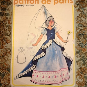 Op de afbeelding: Een vintage naaipatroon getiteld "Patron de Paris" met een illustratie van een prinses in een blauwe jurk met een lange sleep, een puntmuts en een sterrenstaf. Het patroon is voor de leeftijden 6-8-10 jaar.