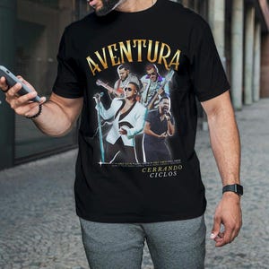 May include: Black t-shirt with a graphic of the band Aventura. The graphic features the band members in a concert setting with the text "Cerrando Ciclos" below the image.