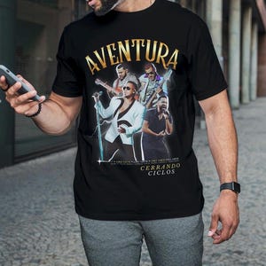 Może przedstawiać: Czarny T-shirt z złotym nadrukiem zespołu Aventura. Nadruk przedstawia członków zespołu i tekst "Cerrando Ciclos".