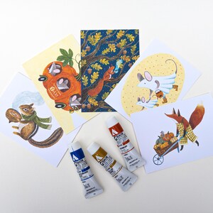 Könnte beinhalten: Eine Sammlung skurriler Illustrationen mit Waldtieren und Herbstmotiven. Die Kunstwerke zeigen ein Eichhörnchen, einen Fuchs und Mäuse, zusammen mit einem Kürbis-Taxi und einer Schubkarre voller Kürbisse. Drei Tuben Gouachefarben in Blau, Gelb und Rot sind ebenfalls vorhanden.
