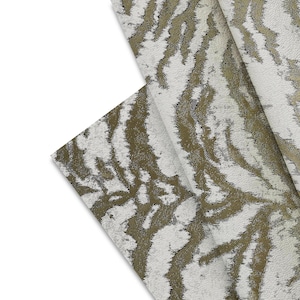 May include: Close-up of a folded fabric with a textured pattern. The design features a white background with a repeating pattern of olive green and silver-colored organic shapes. The fabric is folded over itself, revealing the pattern.