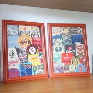 May include: Two orange framed pictures with a collage of vintage beer labels and advertisements. The labels feature various brewery names, logos, and slogans. The pictures are hanging on a wall.
