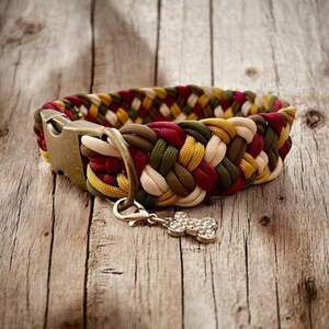 Könnte beinhalten: Ein geflochtenes Hundehalsband in Rot, Grün, Gelb und Creme mit einer Messing-Schnalle und einem Knochen-Anhänger.