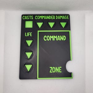 May include: Black and green 3D printed game board with the text "CASTS COMMANDER DAMAGE", "LIFE", "COMMAND ZONE" and green arrow symbols.