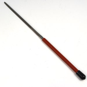 May include: A metal file with a long, slender, tapered steel blade and a cylindrical red handle. The handle features a smooth, solid red finish and is capped with a small, rounded black end piece, providing a secure grip for the tool.