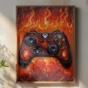 May include: Framed artwork featuring a stylized Xbox controller engulfed in flames. The controller is black and red, with colorful buttons. The background is a fiery blend of orange and red hues, creating a dynamic and energetic visual.