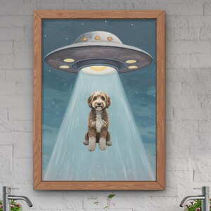 May include: A framed painting of a brown and white dog standing in front of a blue and white UFO. The UFO is emitting a beam of light that shines on the dog.