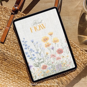 May include: A digital tablet with a white background and a floral design. The text "Floral Flow" is written in a cursive font on the screen. The tablet is lying on a woven straw mat.