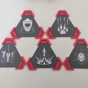 May include: Six gray, triangular coasters with red trim, each featuring a different white graphic design. The designs include a heart, paw print, three vertical lines, an arrow, a burst, and a skull. These coasters are likely for a game or themed collection.