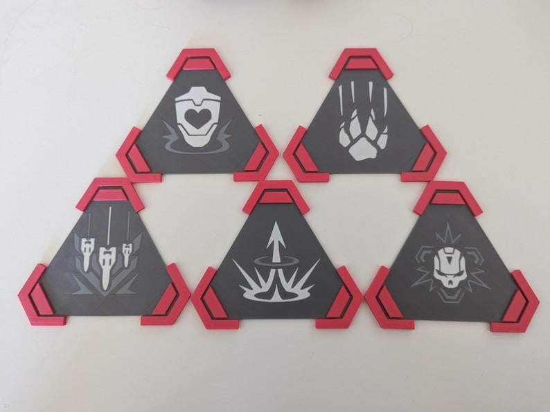 May include: Six gray, triangular coasters with red trim, each featuring a different white graphic design. The designs include a heart, paw print, three vertical lines, an arrow, a burst, and a skull. These coasters are likely for a game or themed collection.