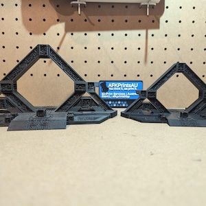 May include: Two black, geometric structures with pyramid-like shapes and intricate details. The structures have a square opening at the top and a base with steps. A business card is visible in the background.