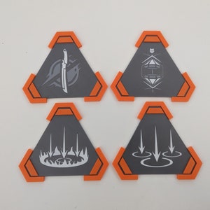 May include: Four gray, triangular game pieces with orange accents. Each piece features a unique white graphic: a knife, a geometric design, a flame-like shape, and arrows. The pieces are arranged on a white surface.