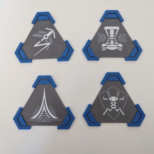 May include: Four gray, triangular coasters with blue trim. Each coaster features a different white graphic design: a stylized arrow, a vehicle, a tower, and a robot. These coasters are ideal for protecting surfaces from drink condensation.