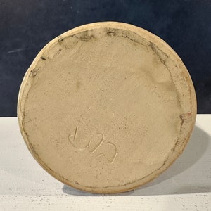 Op de afbeelding: De onderkant van een beige keramische pot met een handgeschreven inscriptie die "L22" luidt.