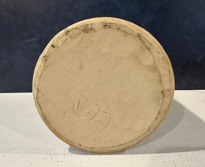 Op de afbeelding: De onderkant van een beige keramische pot met een handgeschreven inscriptie die "L22" luidt.